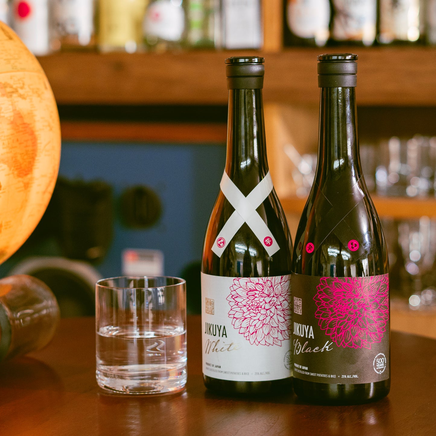 A bottle of Jikuya White (left) sits next to its sibling product, Jikuya Black (right), on the counter in a Japanese bar.